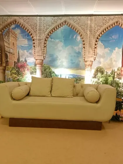 A themed stage backdrop featuring a print of scenic Moroccan arches. The setup is completed with a comfortable sofa and floral arrangements, transporting guests to another place.