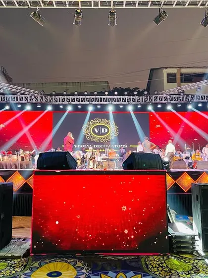 A head-on view of the concert-style stage we built. The setup includes large speaker stacks, a branded DJ booth, and a vibrant red LED backdrop, creating a professional and immersive experience.