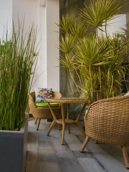 A cozy balcony corner perfect for morning coffee. Wicker chairs and abundant potted plants create a small, private oasis that feels like an escape from the city.