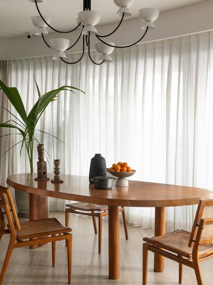 The fondest memories are made around the table. This dining space uses a warm wooden table, cane chairs, and a modern sculptural chandelier to create an earthy yet sophisticated setting.