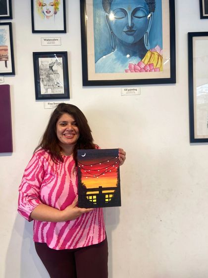 A participant proudly holds up her sunset canvas painting. The satisfaction of creating something with your own hands is a wonderful feeling.