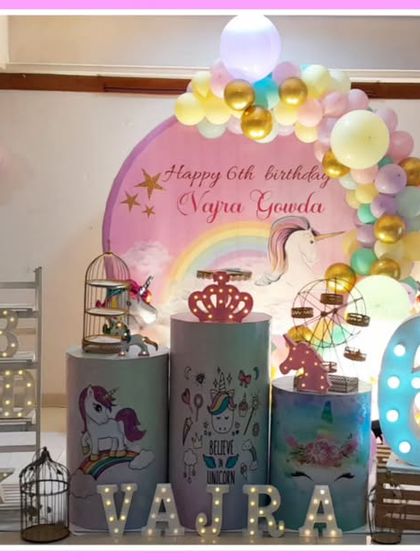 A pastel unicorn-themed sixth birthday. The setup features unicorn cutouts, a rainbow backdrop, and a large light-up number '6'.