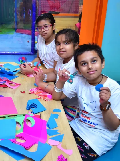 A group of children proudly display their colorful paper creations. Our craft sessions focus on developing fine motor skills with activities like cutting, pasting, and assembling their own unique art.