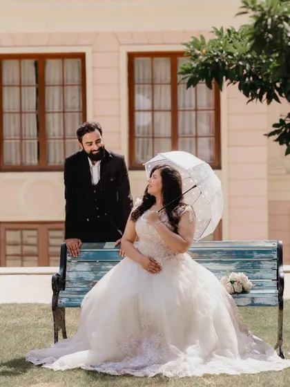 A playful and romantic shot on the bench, with the groom looking lovingly at his bride. The umbrella adds a charming, whimsical touch.