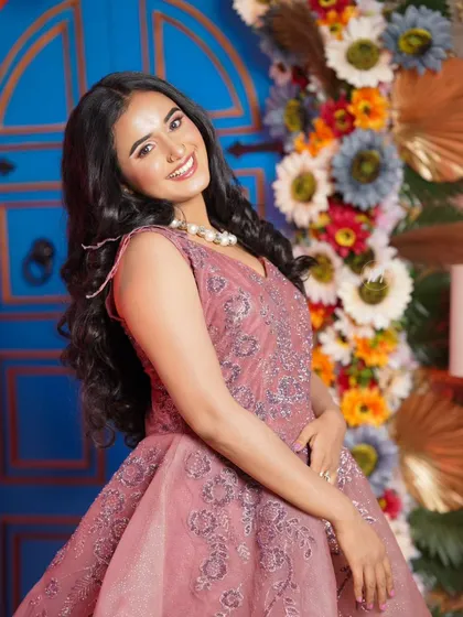 A smiling portrait in a pink gown, with a beautiful floral background. The makeup is fresh and youthful.