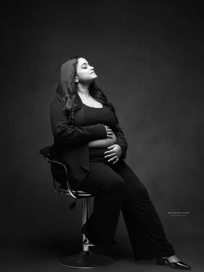 A powerful and confident black and white portrait. The mother-to-be is styled in a modern pantsuit, showcasing a different, boss-mom side of maternity.