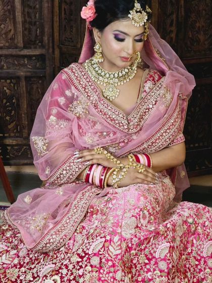 A seated view of the bride in the pink and red velvet lehenga, showing the intricate floral embroidery on the skirt.