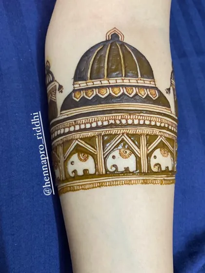 This arm cuff features a popular dome-style design. The intricate architecture is detailed with small elephants, creating a regal and trending look for the start of a bridal henna design.