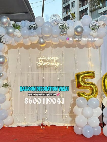 A simple and elegant 50th birthday setup for an outdoor party. The white and silver balloon arch against a white curtain is timeless.