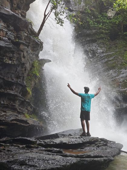 Arms wide open to embrace the beauty of an unexplored waterfall. This is the kind of rewarding moment our offbeat treks deliver.