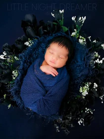 A newborn dreams among dark blue and white flowers. This artistic composition creates a beautiful contrast and a magical, night-sky feeling for an infant portrait.