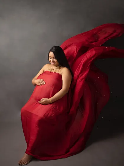 A dramatic solo portrait in a vibrant red gown. The flowing fabric creates a sense of movement and power, beautifully highlighting the baby bump.