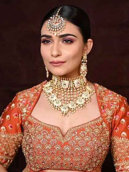A straight-on view of this stunning bridal look. The makeup is balanced, with defined eyes and a soft lip, allowing the outfit and jewelry to take center stage.