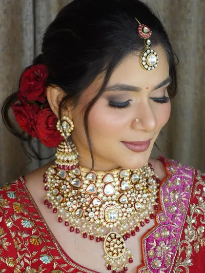 A close-up of a classic bridal makeup look with smoky eyes, nude lips, and a beautiful red floral bun.