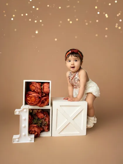 A look of sweet surprise. This little one is celebrating her first birthday in style with a chic studio setup featuring a light-up "1" and beautiful rust-colored flowers.