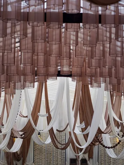 A full view of the ceiling treatment, showing the combination of sheer brown lamp shades and flowing drapes in mocha and cream tones.
