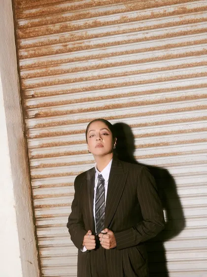 A full-body shot against a rustic shutter, where the strong silhouette of the suit creates a striking contrast.