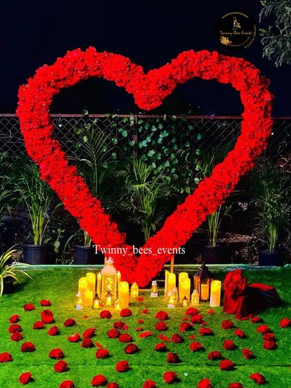 The ultimate romantic setting. We created a large heart-shaped arch of red flowers on a lawn, surrounded by scattered rose petals and glowing electric candles for a magical evening.