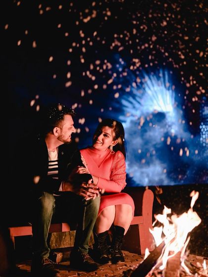 A cozy and romantic shot of a couple sitting by a bonfire with dramatic backlighting and spark effects. This setup is perfect for capturing warm, intimate moments during a night shoot.