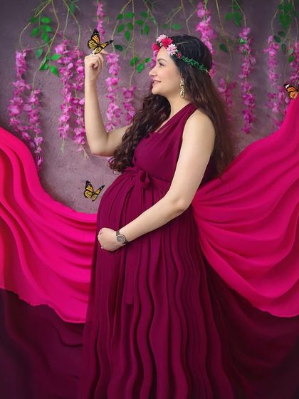 Feeling like a goddess in this whimsical studio setup. The flowing magenta gown, flower crown, and magical butterflies create a truly enchanting maternity portrait.
