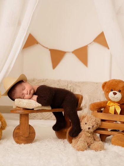 A newborn sleeps on a wooden bench surrounded by a family of teddy bears in a cute, teepee-themed setup.
