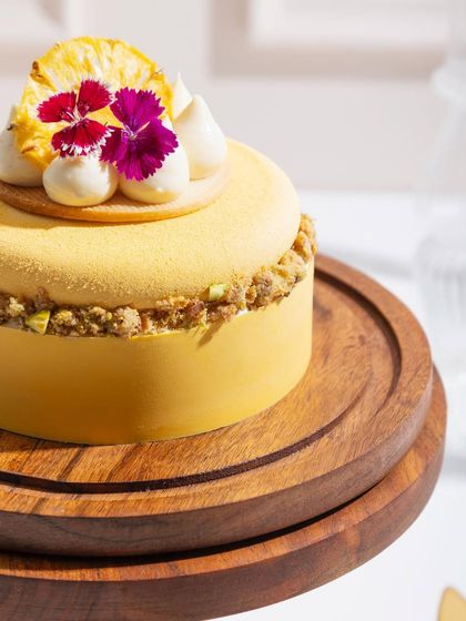 Not your ordinary Lemon and Pineapple cake. This elegant dessert features a velvety yellow finish and is adorned with edible flowers and a dried pineapple slice.