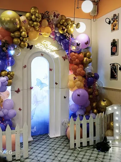 A beautiful butterfly garden theme for a first birthday. An arched doorway is surrounded by a stunning balloon arrangement in purple, gold, and orange, with delicate butterfly accents.
