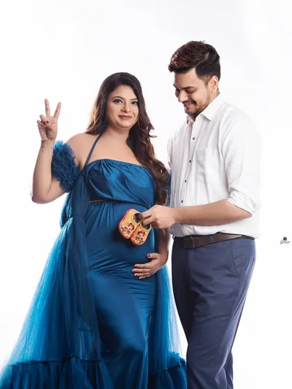 A fun and happy couple's portrait. The mom-to-be makes a peace sign while her partner holds the baby shoes, capturing a moment of pure joy and excitement.