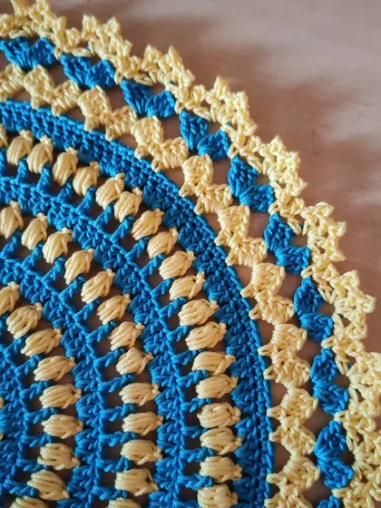 A close-up of the puff stitches and picot edge on the blue and yellow doily.