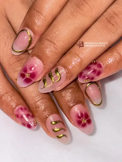 An elegant and artistic design featuring a translucent base with hand-painted magenta flowers, accented with delicate gold swirls and outlines on almond-shaped nails.