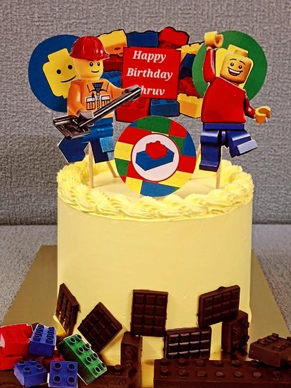 Let's build a fun birthday with this Lego themed cake. It's decorated with edible Lego blocks made from chocolate and features playful Lego character toppers, making it a creative choice for a child's party.
