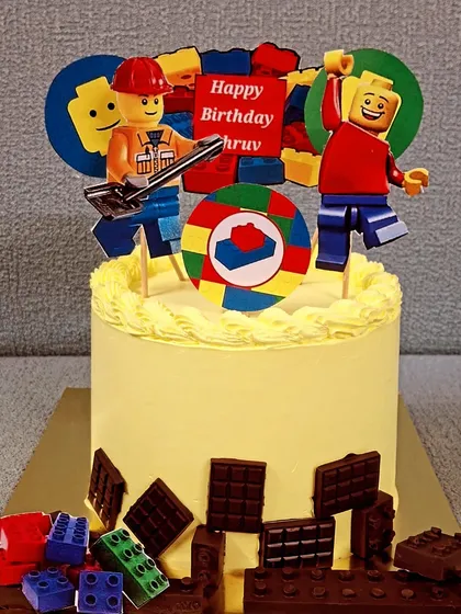 Let's build a fun birthday with this Lego themed cake. It's decorated with edible Lego blocks made from chocolate and features playful Lego character toppers, making it a creative choice for a child's party.
