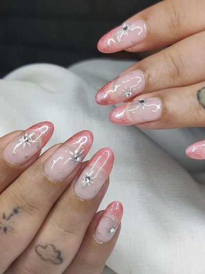 A delicate and sparkly design featuring a pink glitter fade, sheer base, and hand-painted silver sunbursts with rhinestone centers.