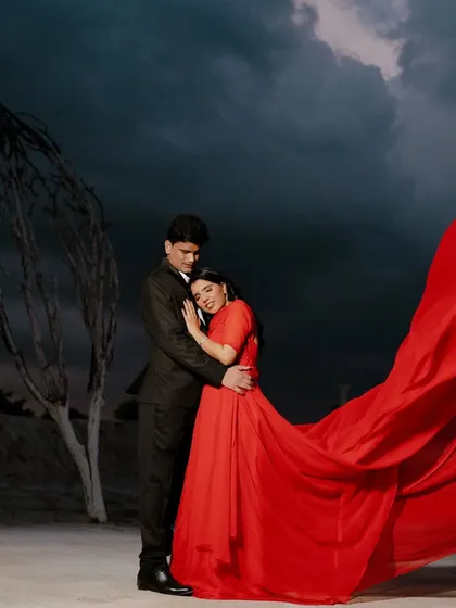 This wide shot shows the full, magnificent sweep of the red gown against the dark sky and stark landscape. It’s a cinematic and unforgettable pre-wedding photograph.