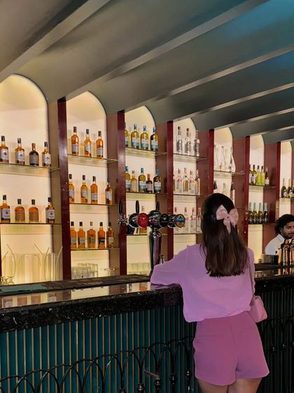 A candid shot at the bar. The soft pink bow in my hair ties the whole look together, proving that small accessories can make a big difference.