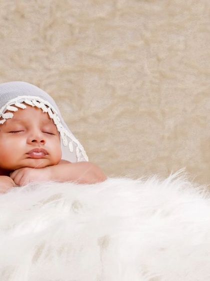 A serene portrait of a baby with a delicate white lace veil draped over their head, resting on a cloud of white fur.