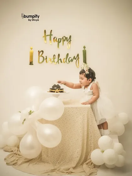 Reaching for the cake! This classic white and gold themed birthday setup is perfect for capturing that moment of curiosity before the smashing begins.