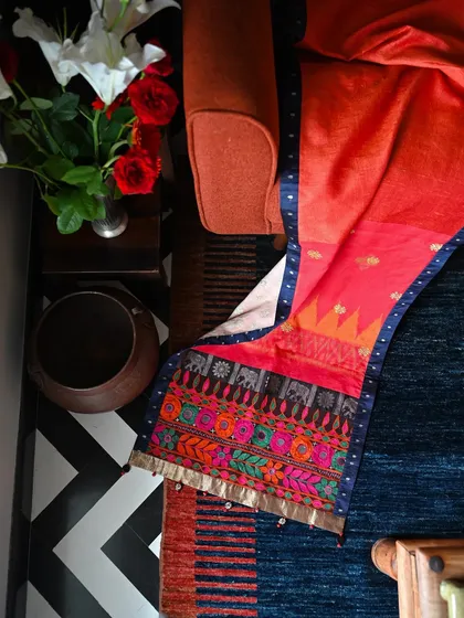 A silk runner that combines two distinct textile traditions: Balinese Endek Ikat and tribal Banjara embroidery from Kutch. The vibrant red of the hand-loomed Balinese fabric is grounded by the earthy, intricate embroidery.