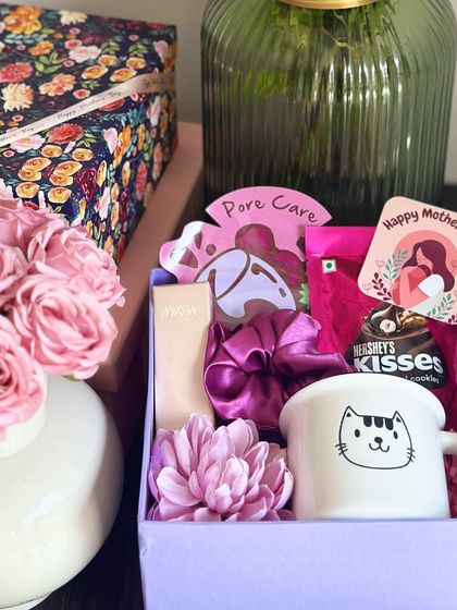 A lavender-themed Mother's Day hamper, featuring a cute cat mug, Hershey's Kisses, a Nykaa pocket perfume, and a face sheet mask.
