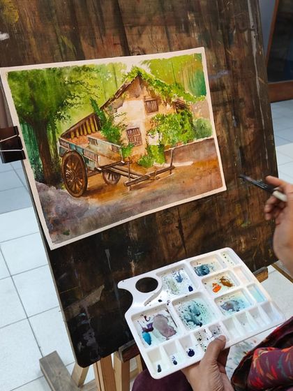 Another angle of the artist's setup, showing her palette and the artwork on the easel, giving a full picture of the creative process.