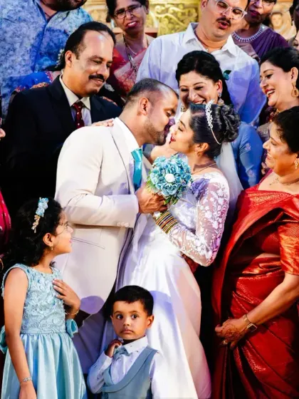 A beautiful, layered group portrait, with the couple sharing a kiss while surrounded by their loving family and friends.