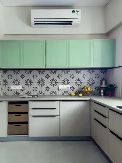 A bright and airy L-shaped kitchen with mint green upper cabinets and off-white lowers. The patterned tile backsplash adds a unique personality to the space, which also includes a tall unit for an oven and microwave.
