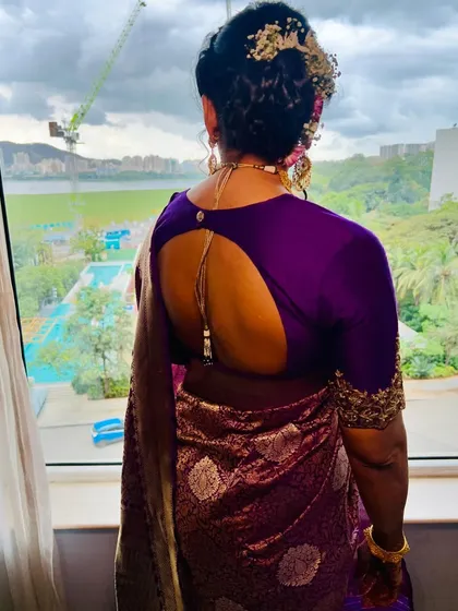 A view of the complete look from the back, showing the elegant braided bun with floral details. The hairstyle and makeup work together to create a polished and traditional look.