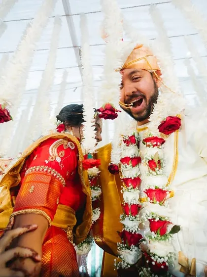 The pure joy of the varmala exchange in a fusion wedding. The low-angle shot captures the excitement and laughter as the couple is surrounded by a canopy of flowers.