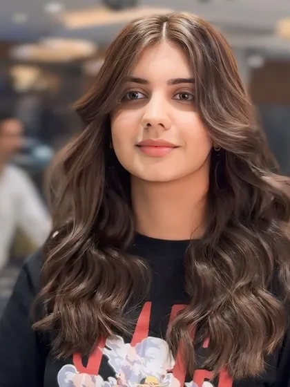 A beautiful portrait of our ash brown hair color. Styled with soft waves and a center part, this look features face-framing layers that highlight the client's features.
