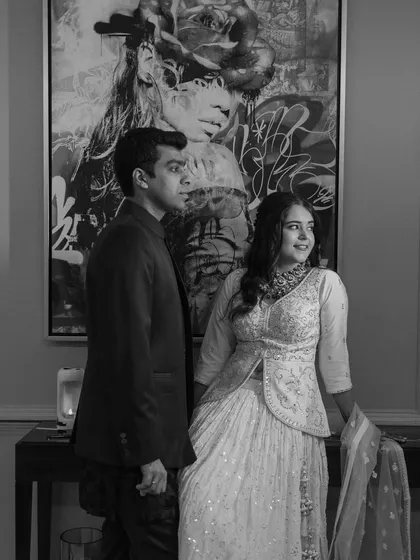 A classic black and white portrait of a couple standing before a large piece of art. Their elegant pose creates a sophisticated and timeless image.