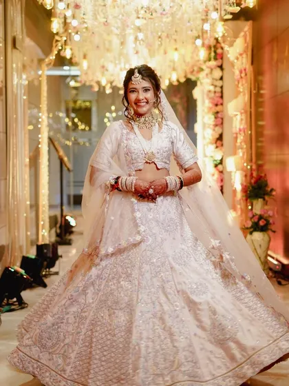 A joyful, full-length shot of the bride in her magnificent white lehenga. The makeup is designed to be bright and radiant, matching the celebratory and grand atmosphere of her wedding venue.