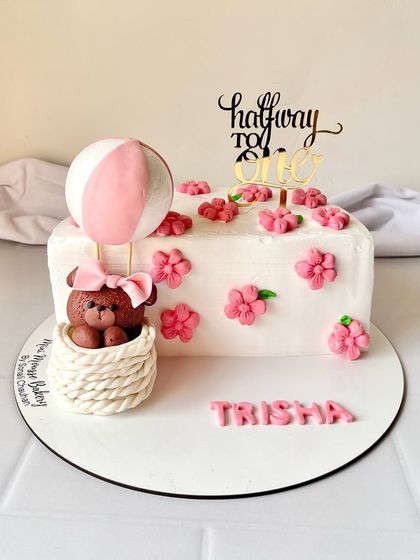 A 'halfway to one' cake for a six-month celebration. This adorable cake features a teddy bear in a hot air balloon, surrounded by pink flowers.
