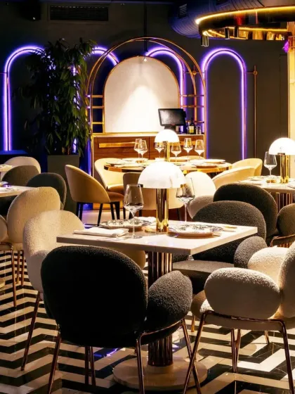 This view showcases the restaurant's seating arrangement, with a mix of small tables perfect for intimate dining. The purple neon-lit arches in the background add a vibrant, contemporary feel.