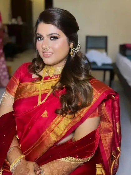 A client styled for a traditional event in a red silk saree. Her hair is in a soft half-updo with curls, a classic choice that complements the rich attire.